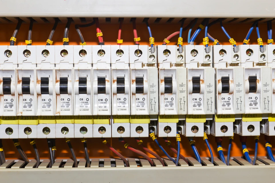 Électricien en combinaison bleue travaillant sur tableau électrique mural blanc