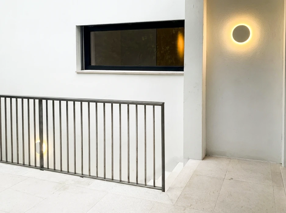 Palier d'escalier intérieur moderne, sol en carrelage travertin clair, garde-corps métallique à barreaux verticaux en acier brut