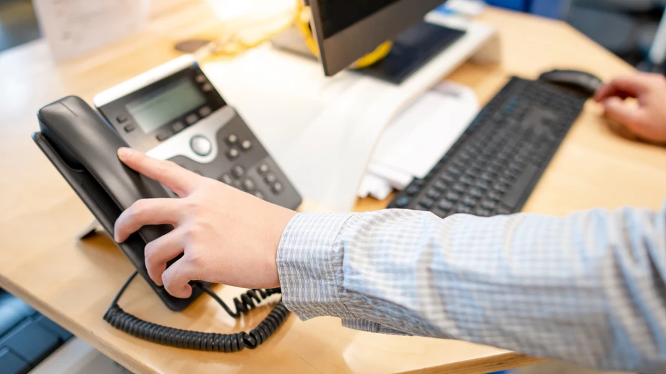 Bureau professionnel avec personne en chemise rayée utilisant téléphone fixe IP moderne à écran LCD