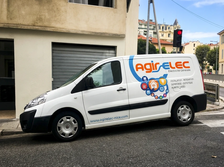 Électricien professionnel en extérieur près de son fourgon utilitaire blanc, portant casque de sécurité blanc et gants de protection