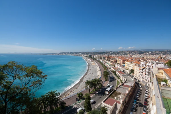 Photographie réaliste d'un électricien en tenue professionnelle complète (uniforme de travail, gilet haute visibilité) intervenant dans un intérieur résidentiel ou professionnel à Nice. L'électricien effectue une installation ou un diagnostic : main sur un boîtier de commande domotique intelligent, un panneau de contrôle, ou posant une prise réseau RJ45. Arrière-plan montrant un intérieur moderne de qualité moyenne à supérieure, typique des habitations niçoises (murs clairs, fenêtre donnant sur la côte ou paysage local visible). Lumière naturelle de jour, photographie style reportage professionnel, composition montrant l'expert à l'œuvre dans son environnement d'intervention local.