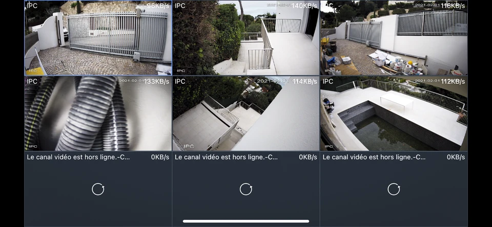 Caméra de surveillance extérieure installée dans un environnement résidentiel avec végétation luxuriante et bâtiments en arrière-plan