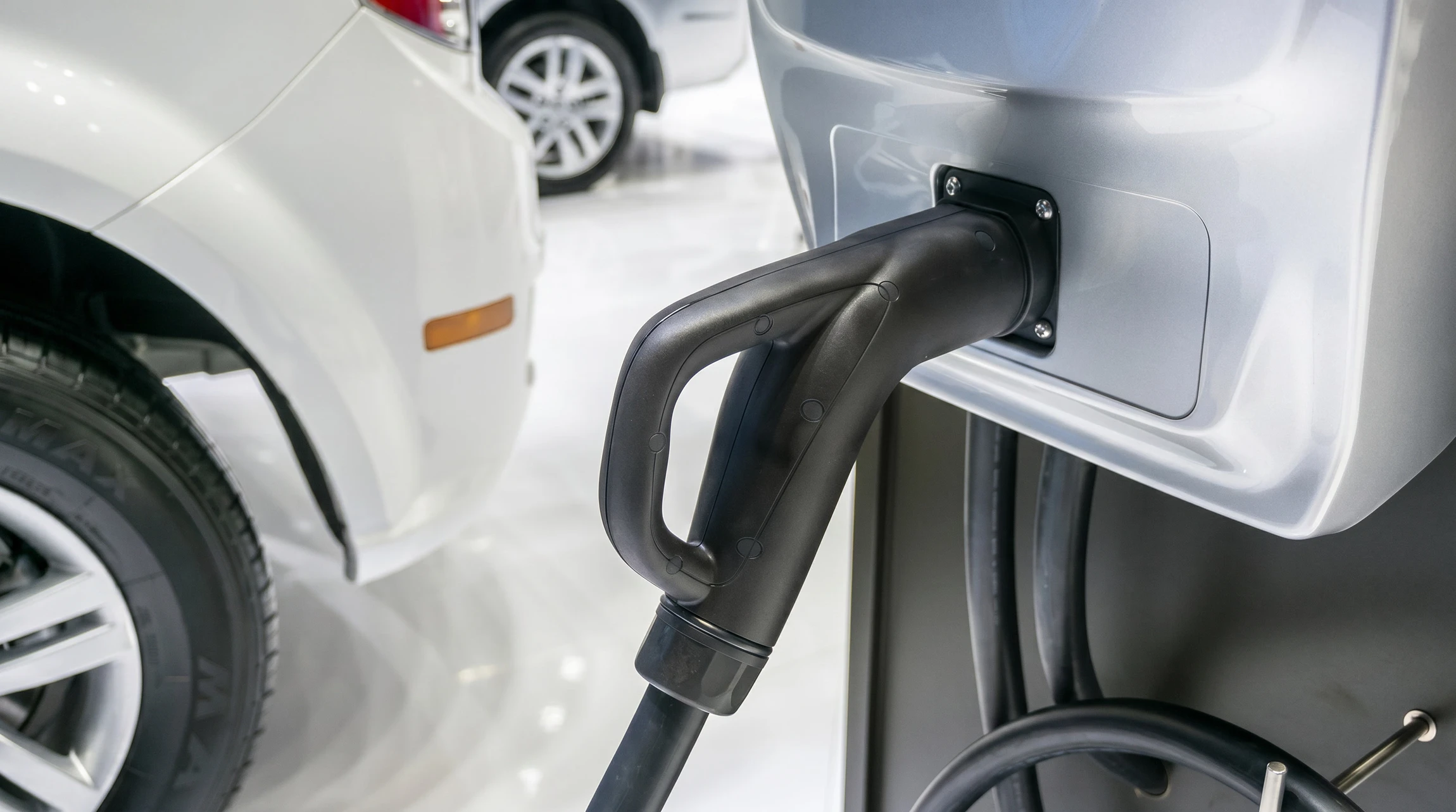 Scène extérieure de recharge d'un véhicule électrique blanc sur parking avec sol carrelé bleu et lignes oranges